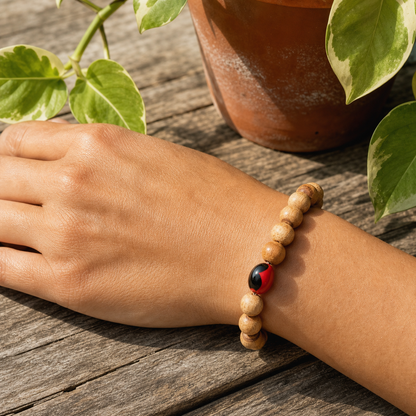 A wooden bead bracelet with a red and black ladybug charm worn on a person's wrist, resting on a weathered wooden surface with a potted plant in the background.
