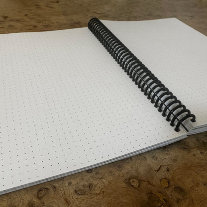 Open Spirit Science Dotted Journal showing blank dot-grid pages and spiral binding on a wooden table.